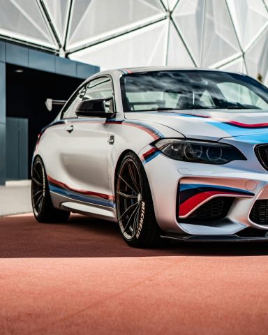 A luxury silver BMW M2 sports coupe with striking design elements, parked in an outdoor modern setting.
