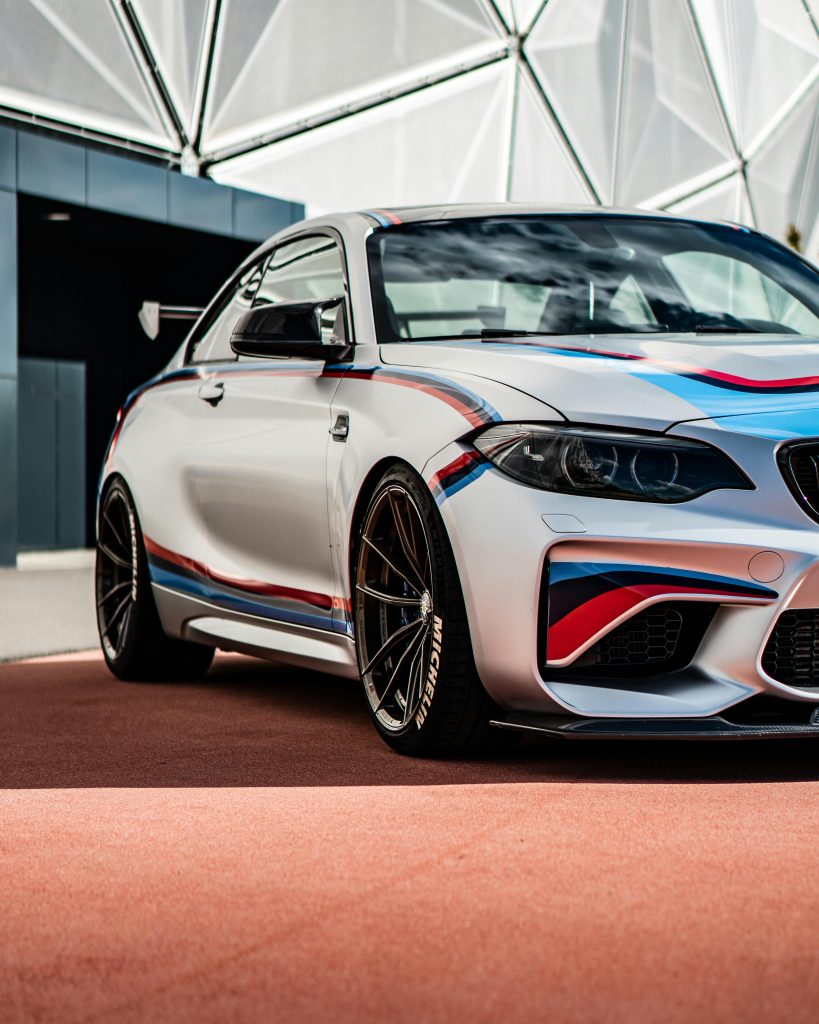 A luxury silver BMW M2 sports coupe with striking design elements, parked in an outdoor modern setting.