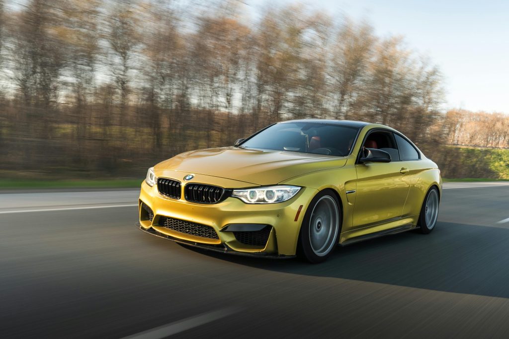 A sleek gold sports car speeds along an open road amidst a natural backdrop, showcasing dynamic motion.