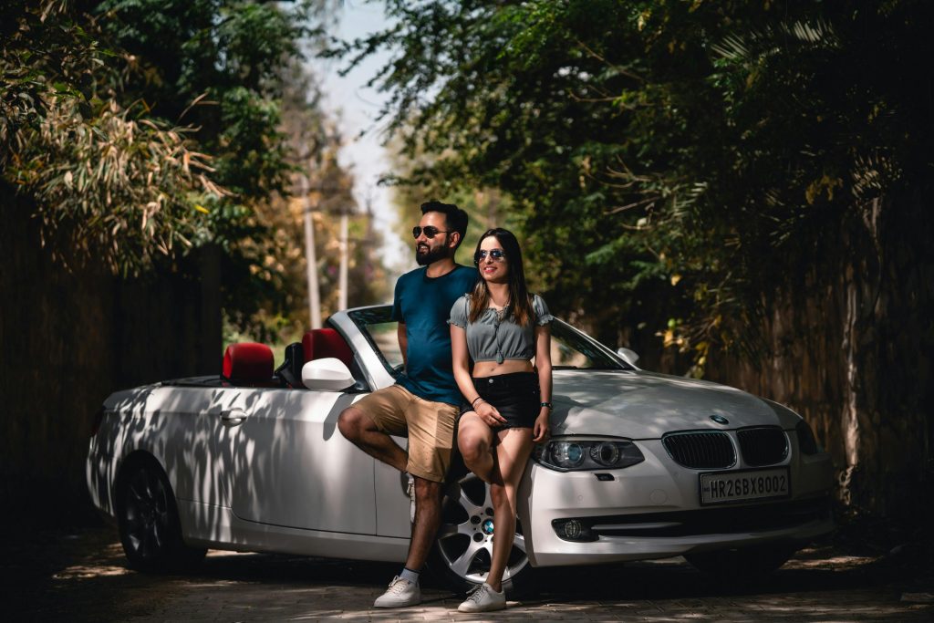 A young couple enjoying a sunny day with their convertible car in Delhi, India.