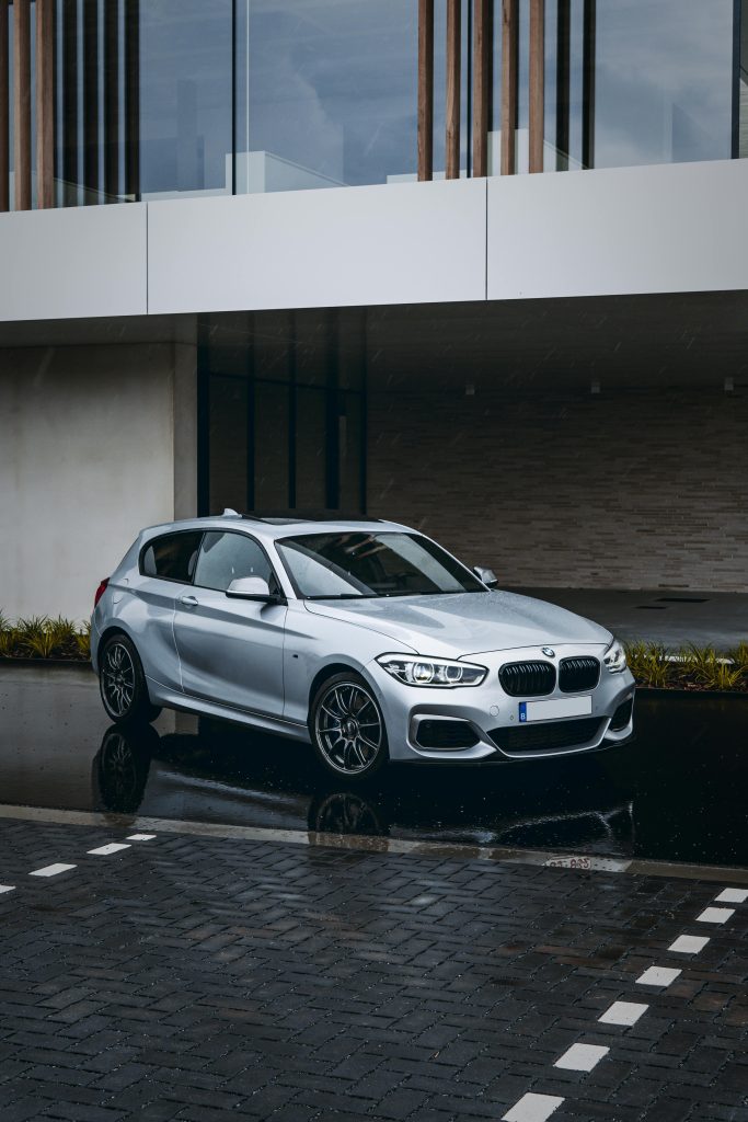 Silver hatchback car parked outside a modern building on a rainy day, reflecting elegance and style.